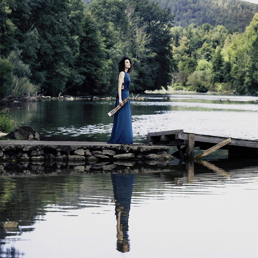 Martina Filjak in a blue gown on a jetty by a lake